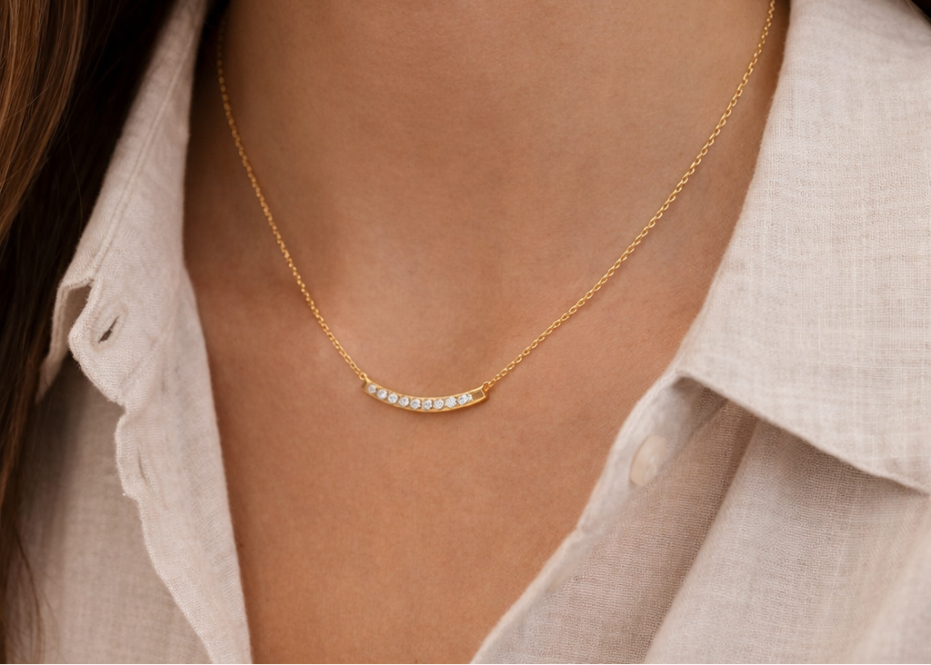 Gold necklace with small diamonds worn by a person in a light-colored shirt.